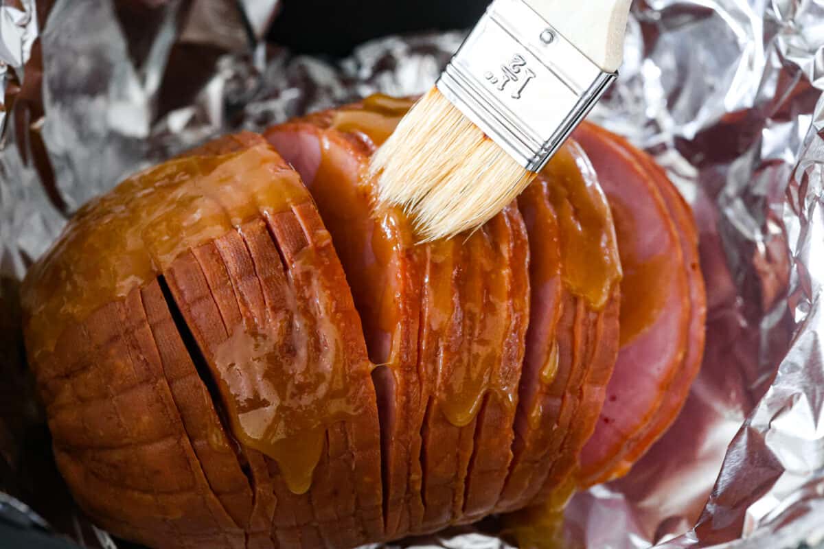 This air fryer ham is moist and flavorful with the most delicious caramelized honey glaze! It's super easy to make and tastes so incredible, you'll never want to cook ham any other way! Your friends and family will all be asking for the recipe! Brushing the air fryer ham with the brown sugar honey glaze.