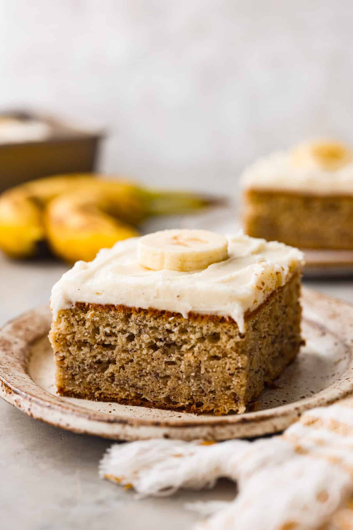 This Banana Cake with Cream Cheese Frosting is light and fluffy with just the right amount of silky smooth frosting on top. If you have overripe bananas, this is the way to use them! A slice of banana cake with cream cheese frosting.