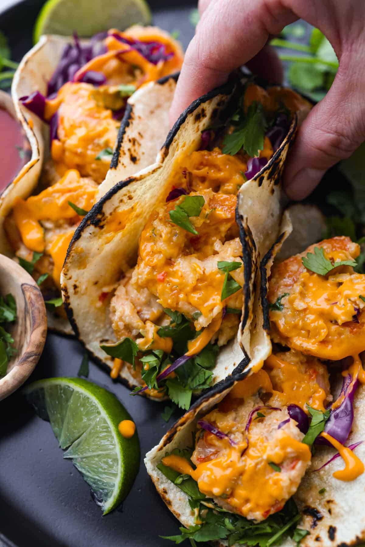 These Bang Bang Shrimp Tacos are made with deliciously crunchy shrimp cooked to perfection and coated in a special sauce that's just bursting with flavor! It's a meal that's sure to impress. A hand holding a bang bang shrimp taco.