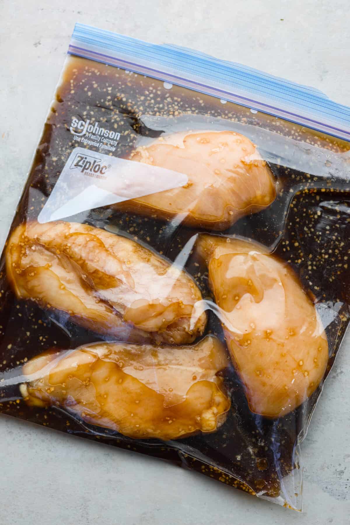 This delicious bourbon marinade will add wonderful depth of flavor and tenderize any meat you're cooking, from steak to chicken! This recipe uses ingredients like brown sugar, Worcestershire sauce, apple cider vinegar, garlic and bourbon to infuse each piece of meat with the perfect savory, sweet and tangy flavor. 4 raw chicken breasts marinating in a bag filled with bourbon marinade.