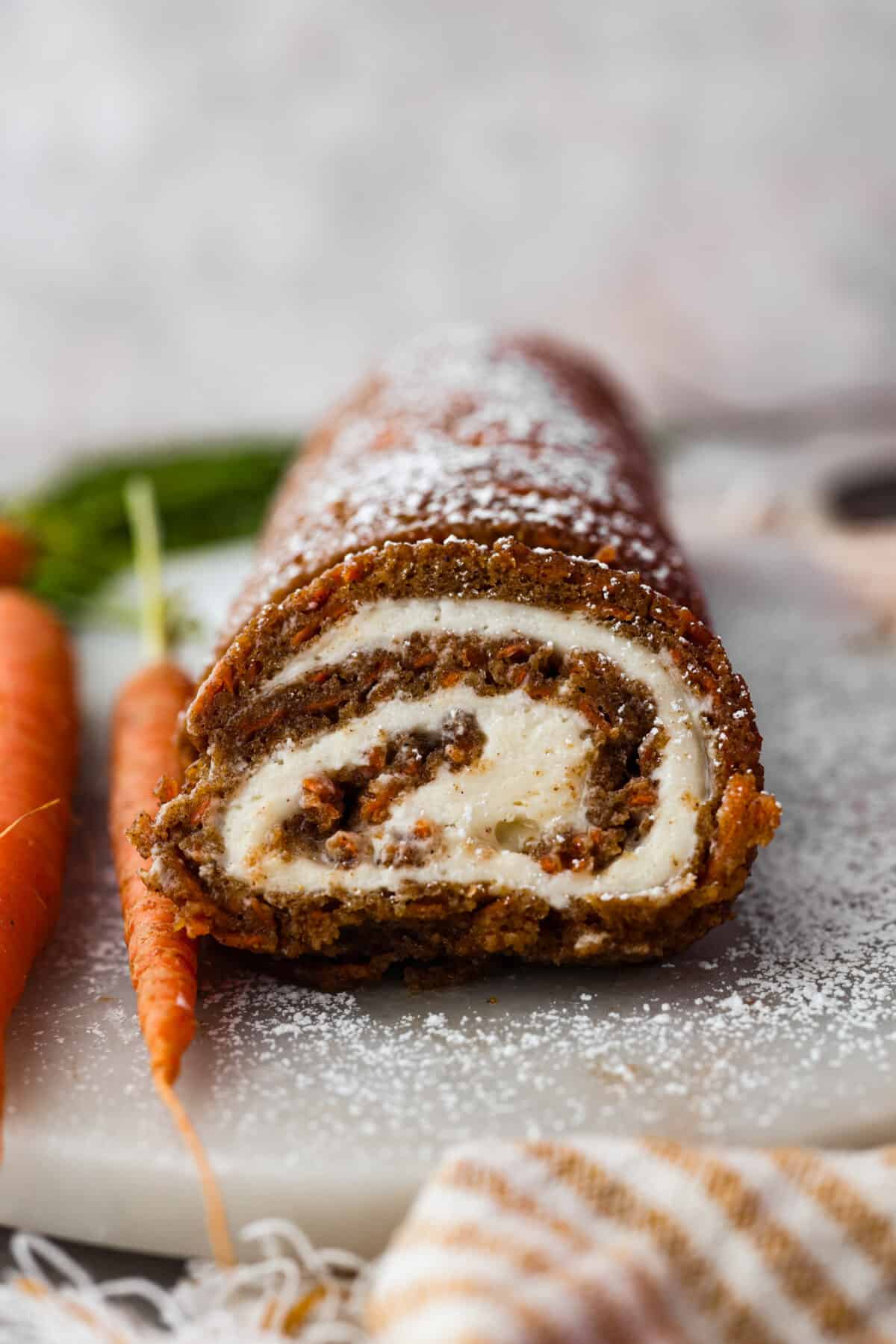 Stunning carrot cake roll is a wonderful joining of deliciously spiced carrot cake, swirled with tangy cream cheese frosting. It looks fancy but it's easy to make and so perfect for Easter and Spring themed celebrations! Front view of a carrot cake roll cut into slices.