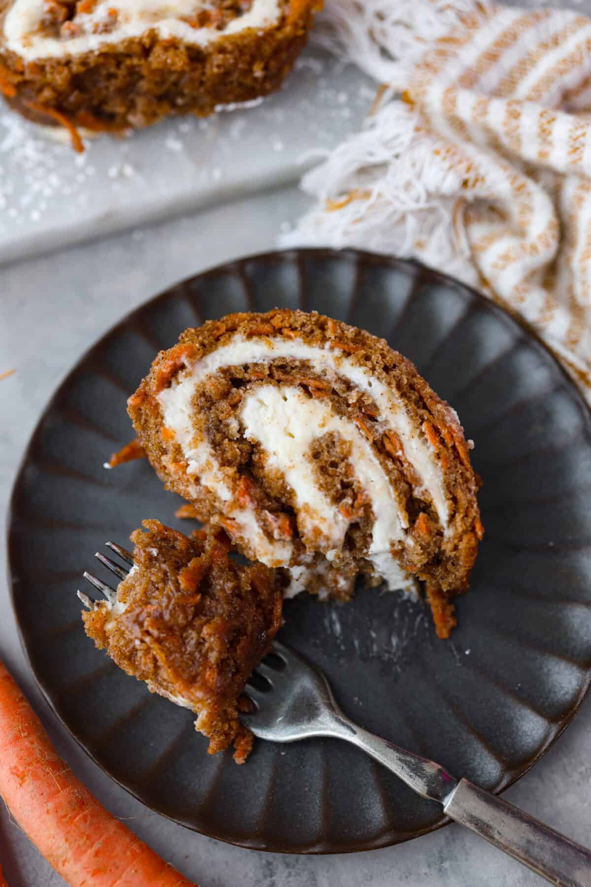 Stunning carrot cake roll is a wonderful joining of deliciously spiced carrot cake, swirled with tangy cream cheese frosting. It looks fancy but it's easy to make and so perfect for Easter and Spring themed celebrations! Taking a bite of cake that was served on a black plate.