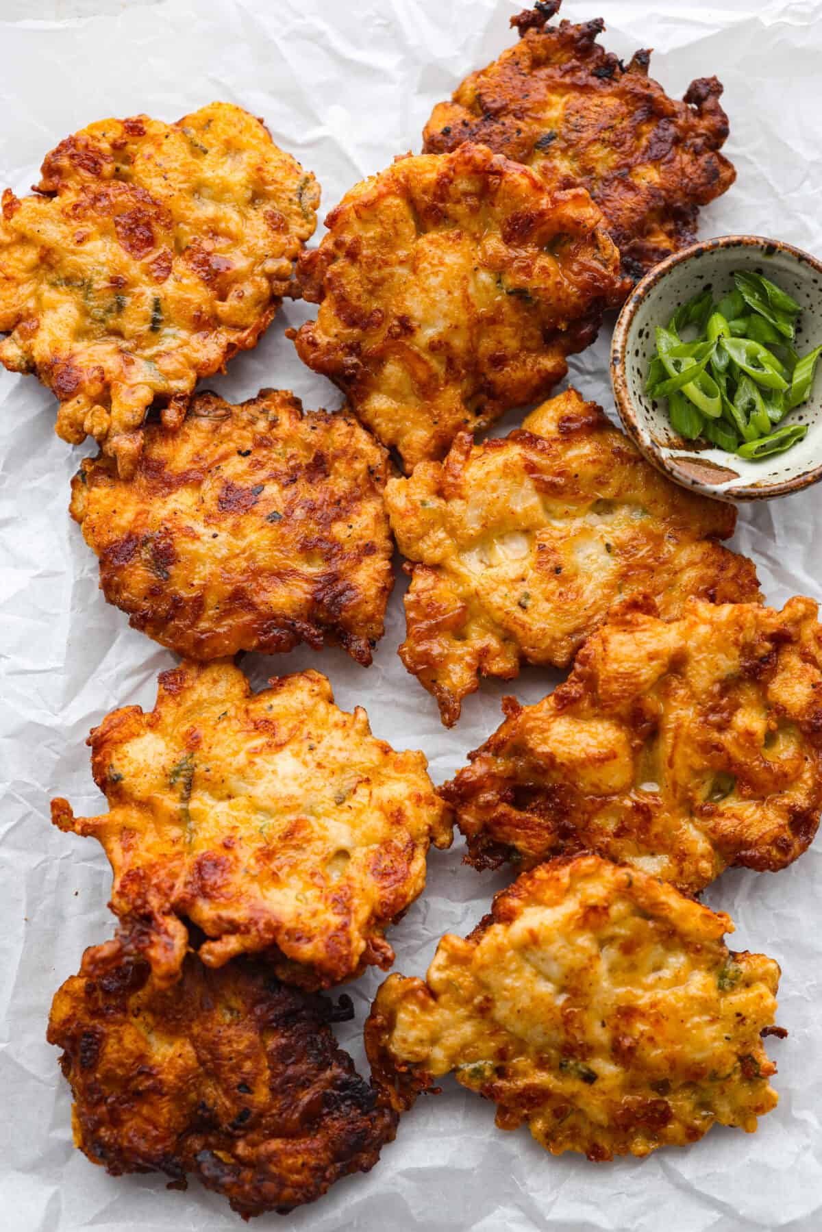 Flavorful chicken fritters are warm and crispy crowd favorites! Simply mix tender pieces of chicken breast and shredded cheese with a seasoned batter and pan-fry to golden brown perfection. Serve them with your favorite sauce and wait for all the rave reviews from your family! Cooked fritters on parchment paper