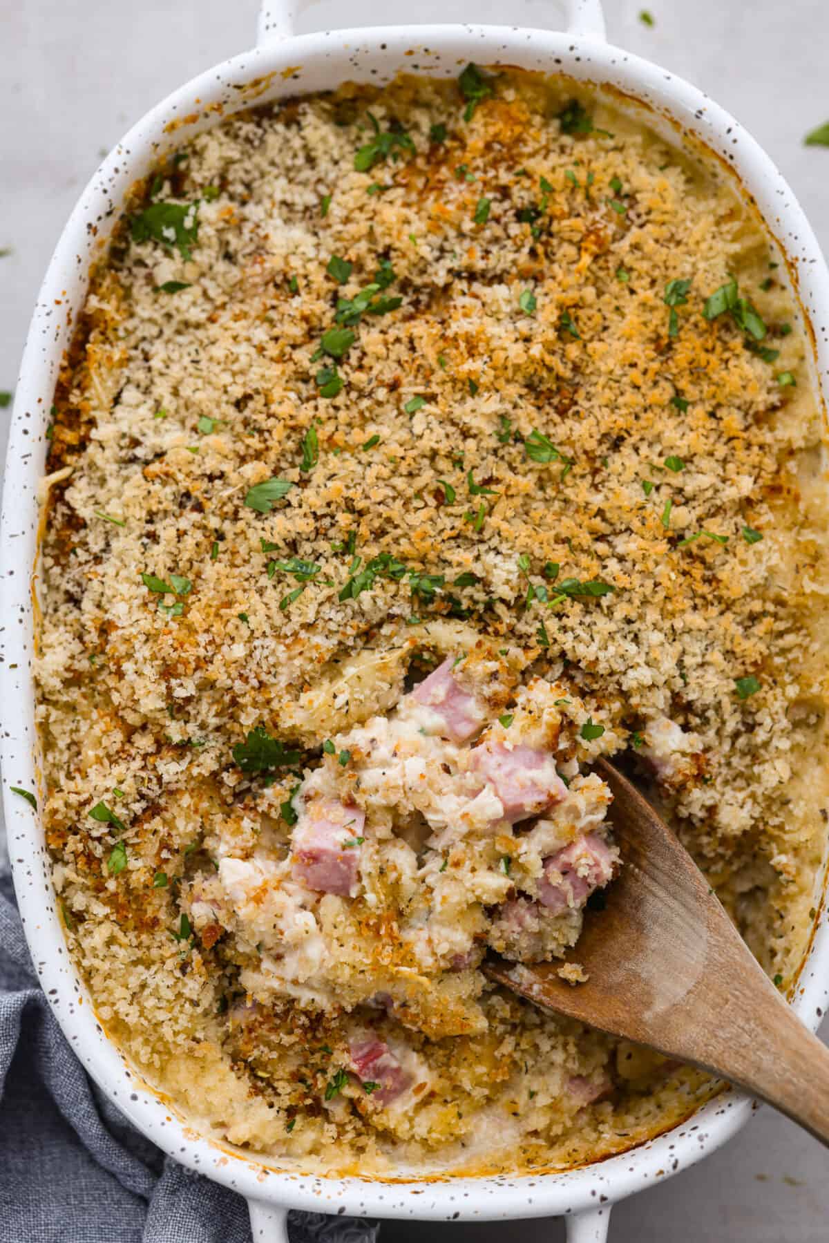 This Chicken Cordon Bleu Casserole is simple and delicious. It combines tender chicken and smokey, flavorful ham in a melty, creamy cheese sauce topped with crispy breadcrumbs. Your whole family will love it! Top-down view of chicken cordon bleu casserole with a scoop being taken out of it.