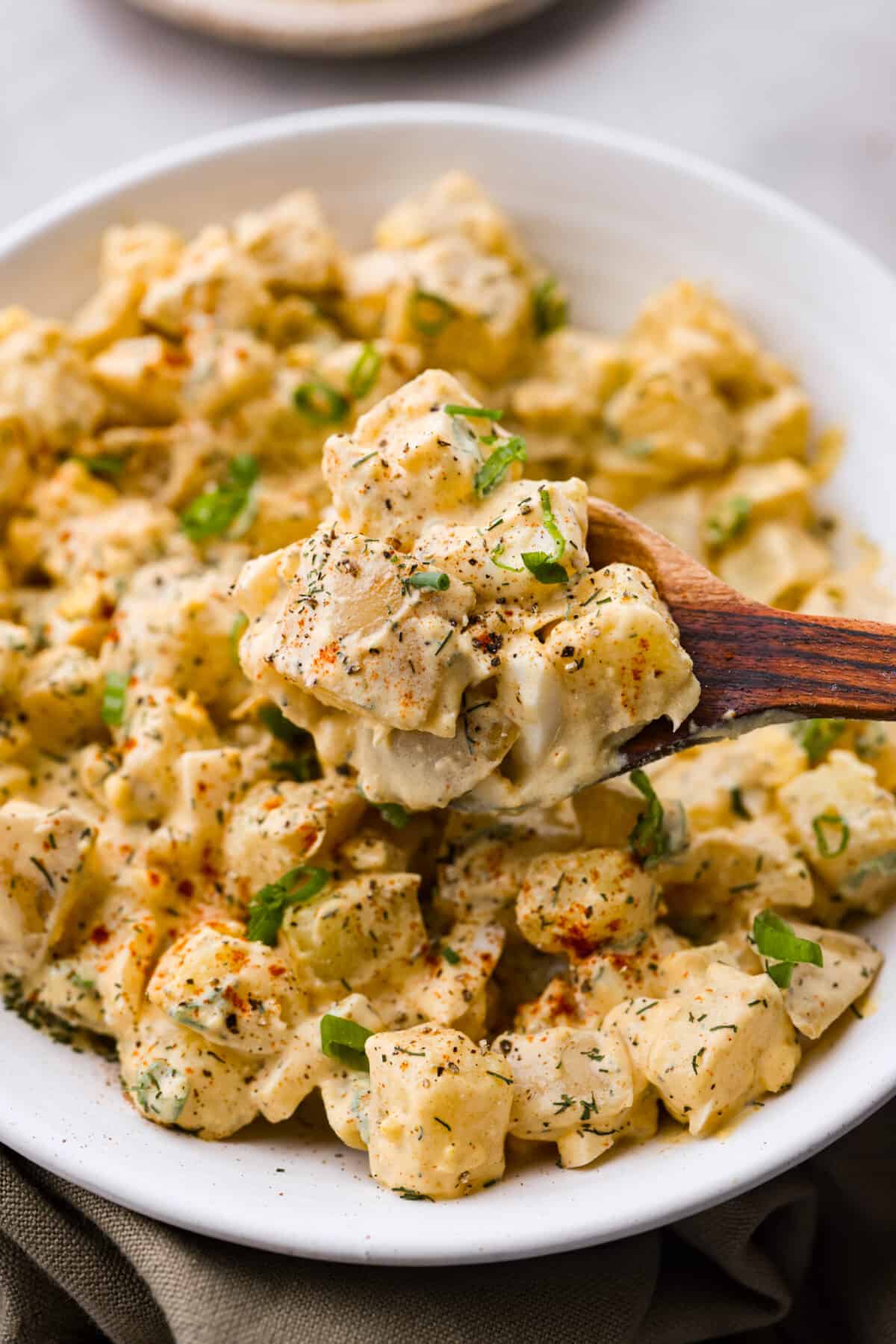This classic potato salad recipe is cool, creamy, and the perfect side dish for any cookout! Easy to make ahead and so flavorful! Closeup of potato salad on a wooden spoon.