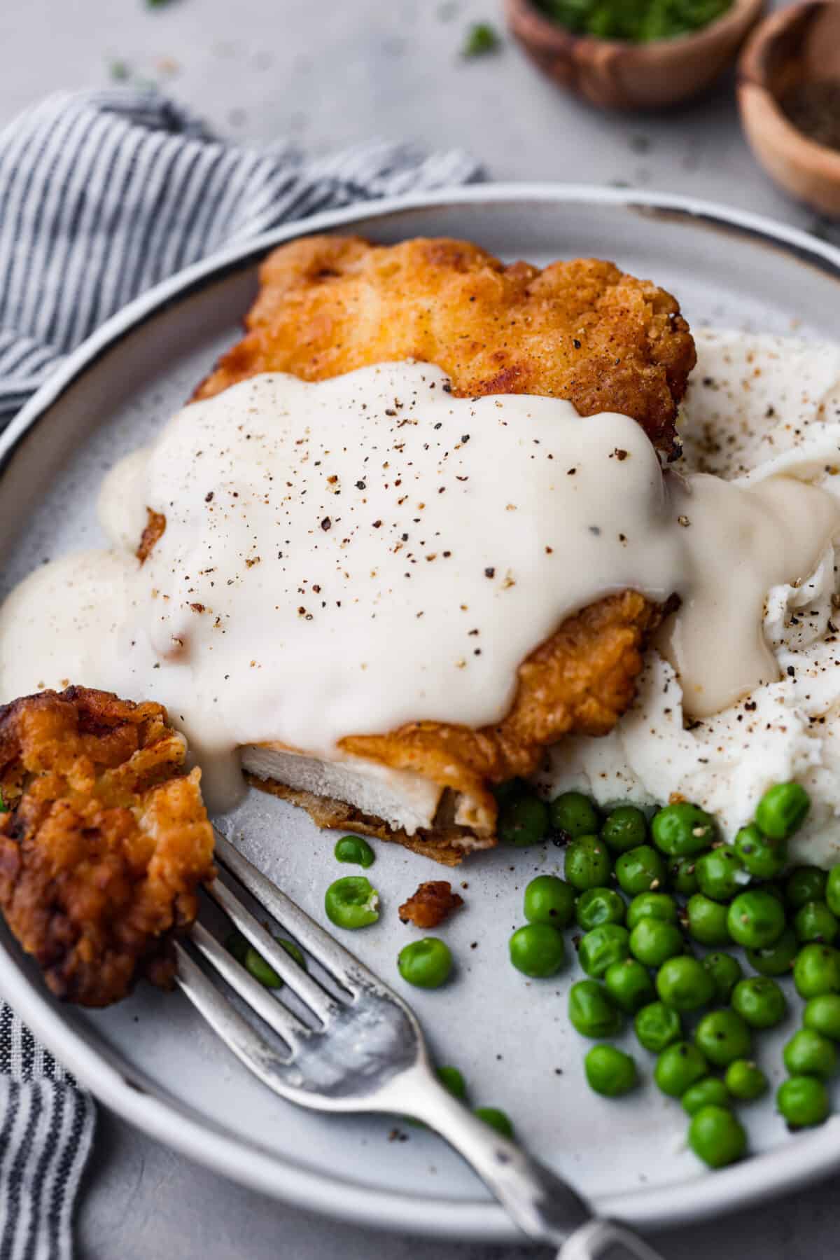Bring all the best things about Southern cooking to your dinner table with this country fried chicken recipe! The result? Golden, crispy goodness smothered in savory homemade gravy. Closeup of country fried chicken covered with gravy and served with peas.