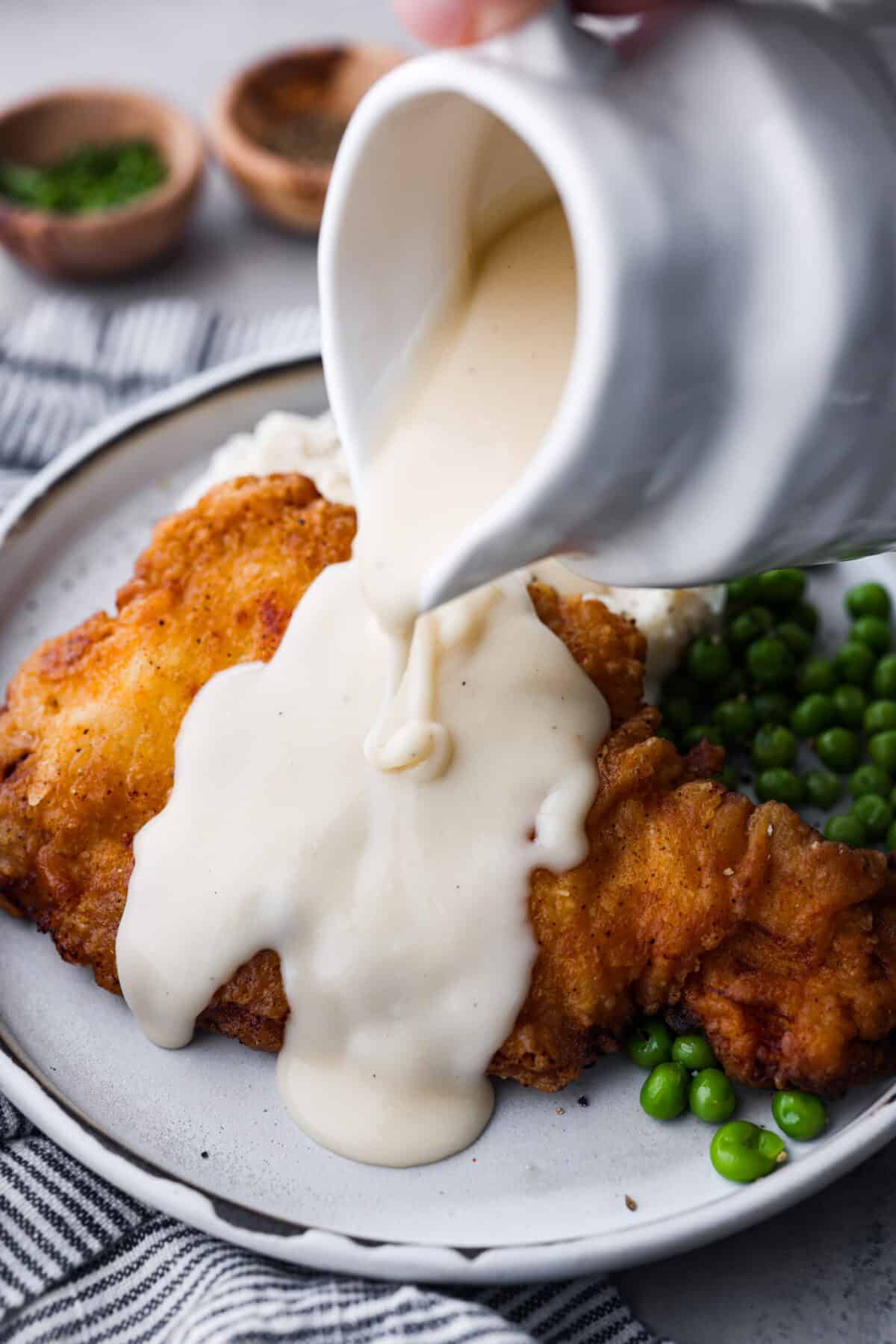 Bring all the best things about Southern cooking to your dinner table with this country fried chicken recipe! The result? Golden, crispy goodness smothered in savory homemade gravy. Pouring gravy over the chicken.