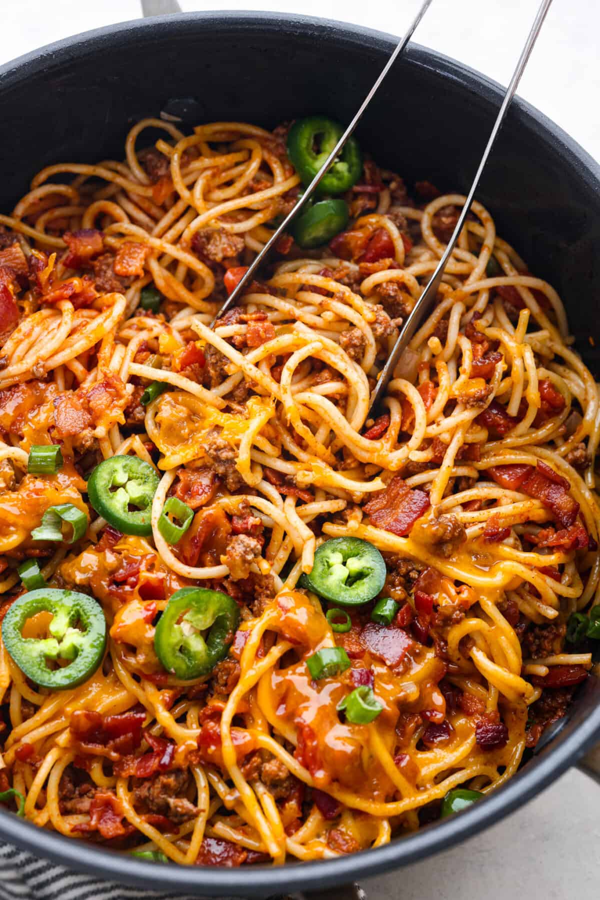 Upgrade your spaghetti with some cowboy fixings: sliced jalapenos, bacon, shredded cheddar cheese, and rotel tomatoes! It’s a hearty American version of a classic dish that everyone will love! Spaghetti topped with shredded cheese, bacon, and jalapenos.