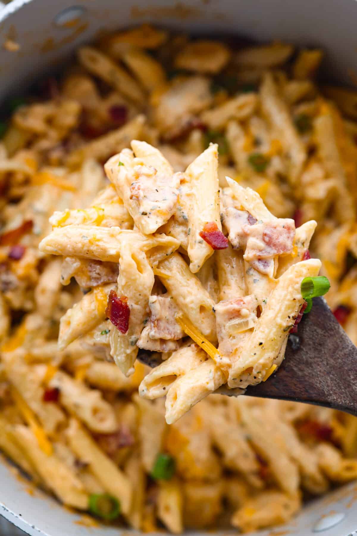 Cheesy, creamy, and loaded with ranch flavor and chunks of juicy chicken, 'Crack Chicken' pasta is a dinner that will have everyone raving! And as if you needed more reason to make it, it's ready in 30 minutes from start to finish! Closeup of crack chicken pasta on a wooden spoon.