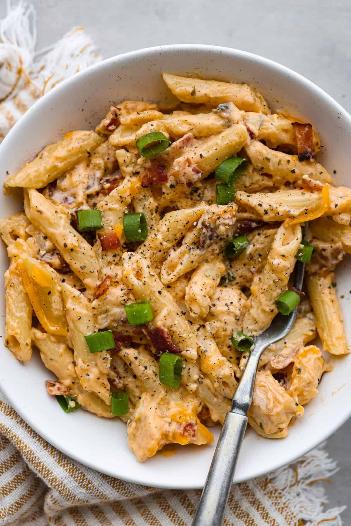 Cheesy, creamy, and loaded with ranch flavor and chunks of juicy chicken, 'Crack Chicken' pasta is a dinner that will have everyone raving! And as if you needed more reason to make it, it's ready in 30 minutes from start to finish! A serving of crack chicken pasta in a white bowl.