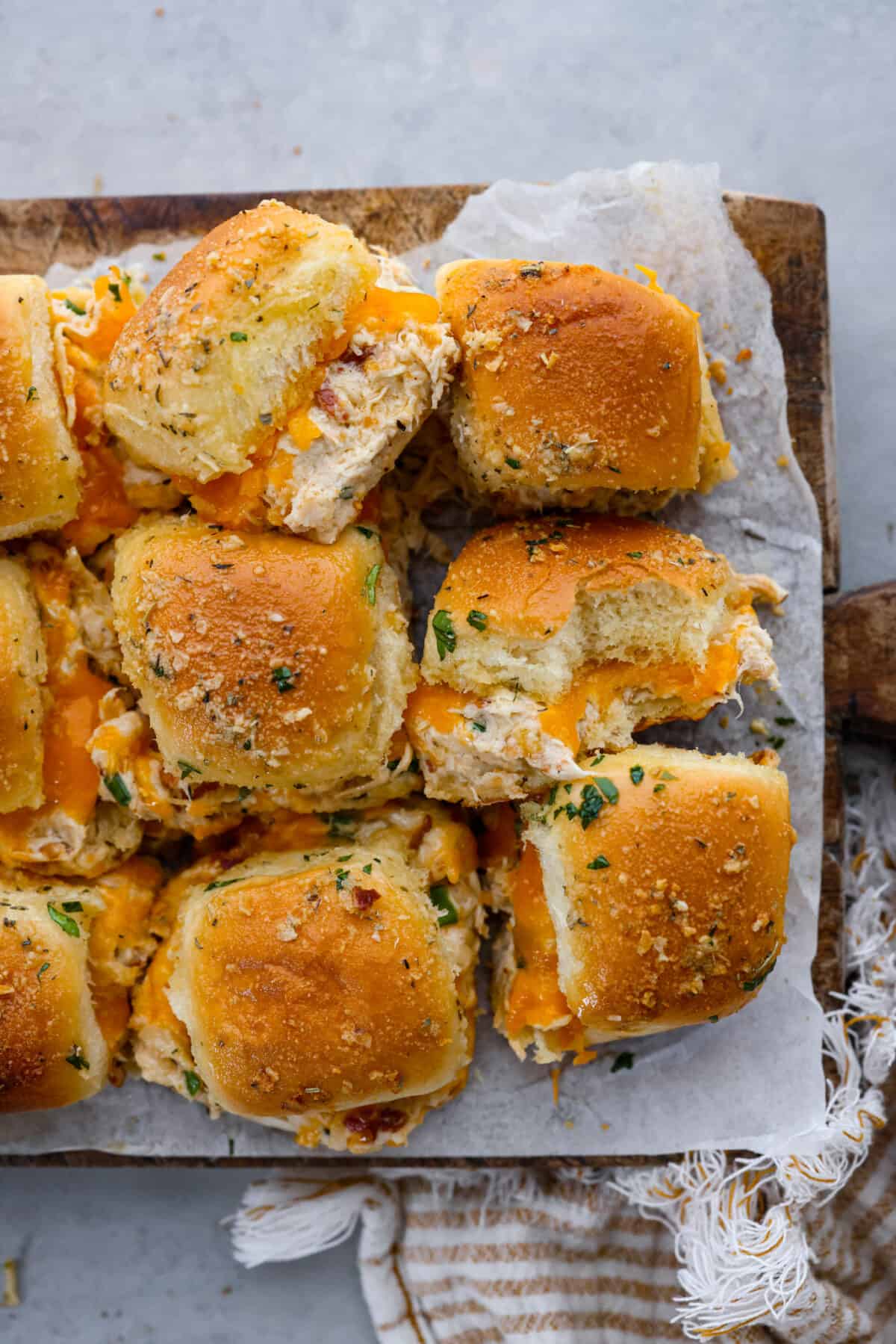 Hawaiian sweet rolls topped with creamy ranch chicken and bacon, brushed with a buttery parmesan glaze and then toasted to golden perfection! The top view of sliders on parchment paper.