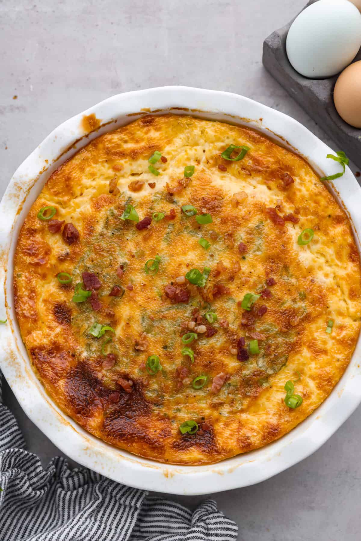 Rich and savory, Crustless Quiche is easy to make with a mix of bacon, green onions, egg custard and cheese, all baked to perfection without the hassle of a pie crust. Fluffy, creamy and filled with incredible flavor, it's great for breakfast or any meal of the day! Top-down view of a baked crustless quiche.