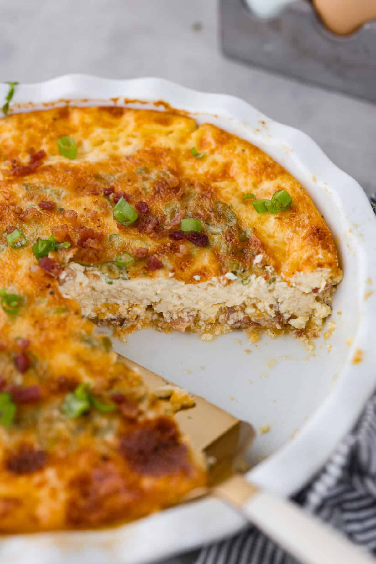 Rich and savory, Crustless Quiche is easy to make with a mix of bacon, green onions, egg custard and cheese, all baked to perfection without the hassle of a pie crust. Fluffy, creamy and filled with incredible flavor, it's great for breakfast or any meal of the day! Quiche with a slice cut out of it.