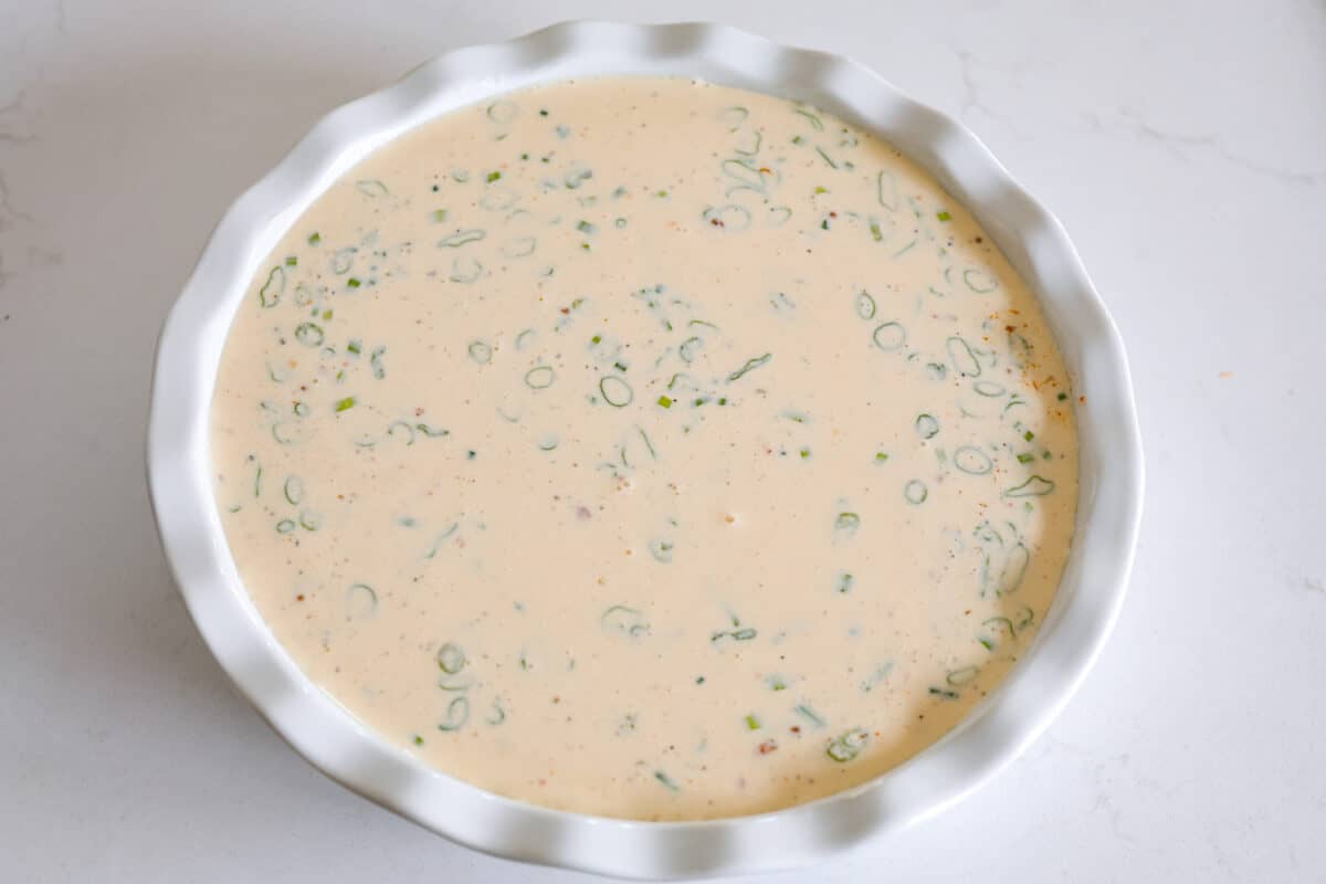 Rich and savory, Crustless Quiche is easy to make with a mix of bacon, green onions, egg custard and cheese, all baked to perfection without the hassle of a pie crust. Fluffy, creamy and filled with incredible flavor, it's great for breakfast or any meal of the day! Adding the quiche mixture into a metal pan.