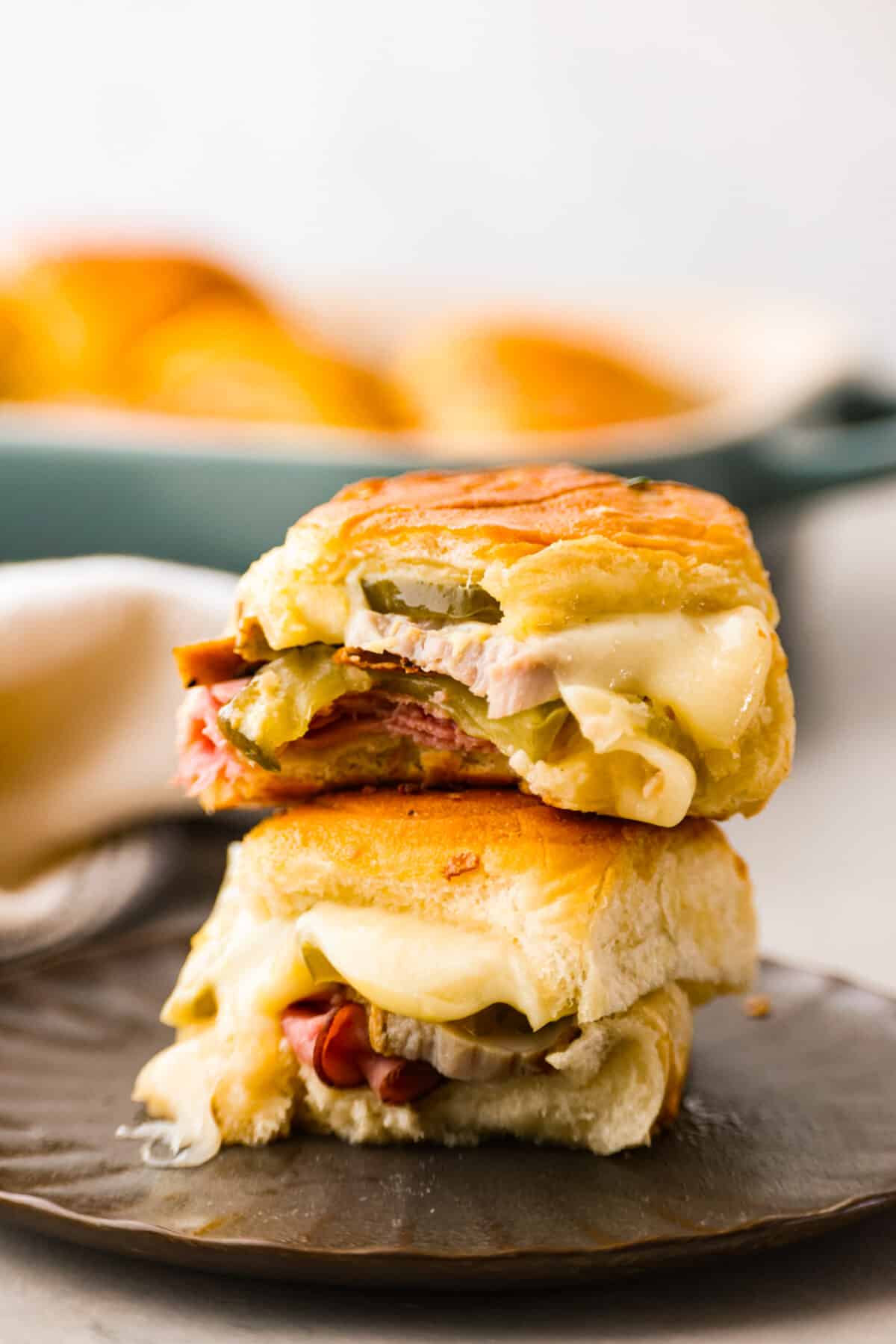 These Cuban Sliders are about to become your new go-to party dish! Think melty Swiss cheese, dill pickles, and all the meaty goodness of a Cuban sandwich, but bite-sized and perfect for sharing. 2 sliders stacked on top of each other.