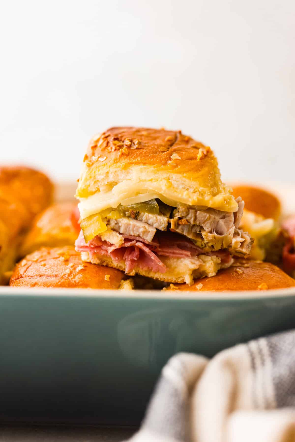 These Cuban Sliders are about to become your new go-to party dish! Think melty Swiss cheese, dill pickles, and all the meaty goodness of a Cuban sandwich, but bite-sized and perfect for sharing. Hero image of a Cuban slider.
