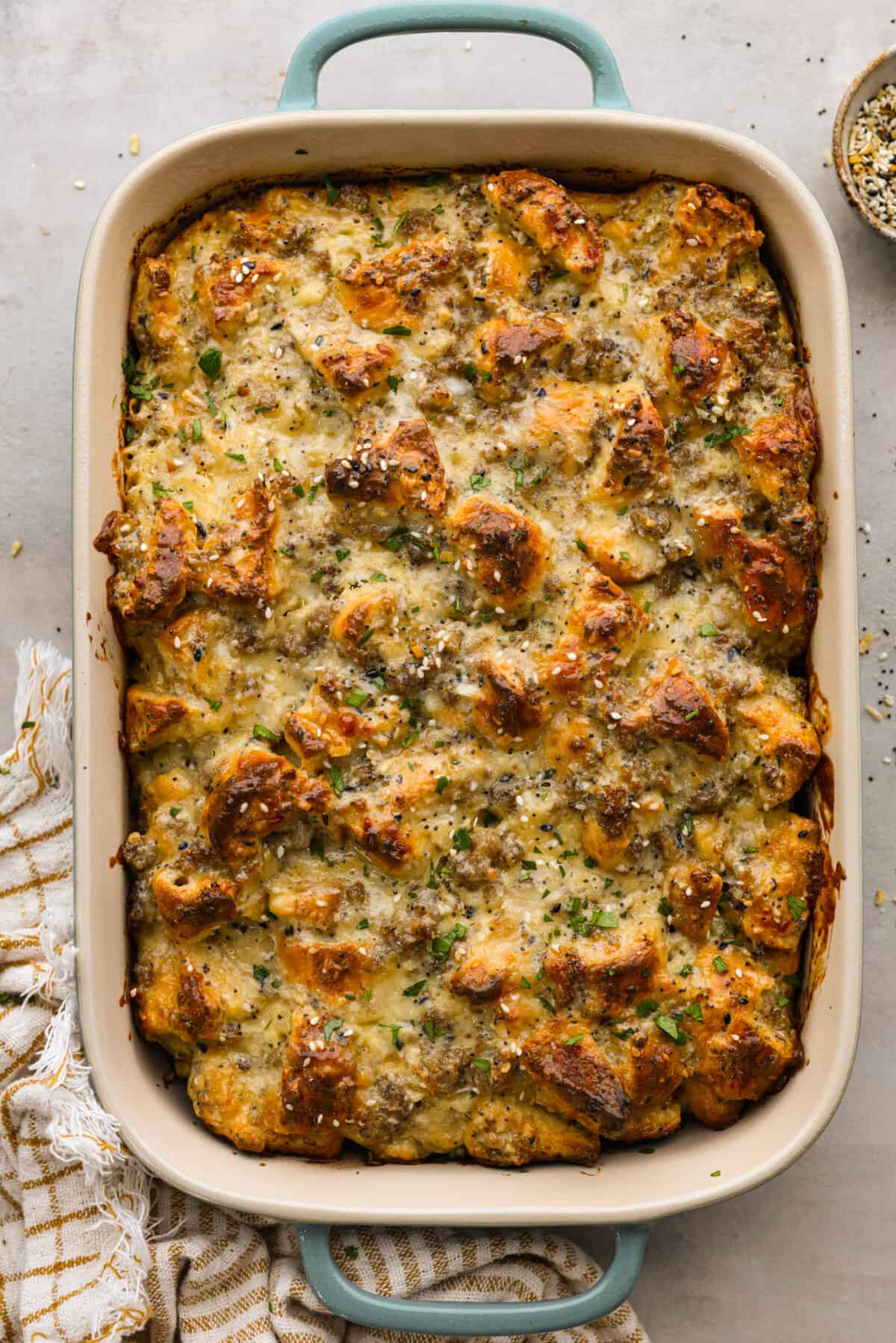 Wake up to the tasty flavors of this everything bagel casserole! It's made with everything bagels and seasoning, sausage, eggs, cream cheese, and gruyère cheese. The result is a creamy and savory breakfast casserole that everyone will devour! Overhead view of everything bagel casserole in a baking dish.