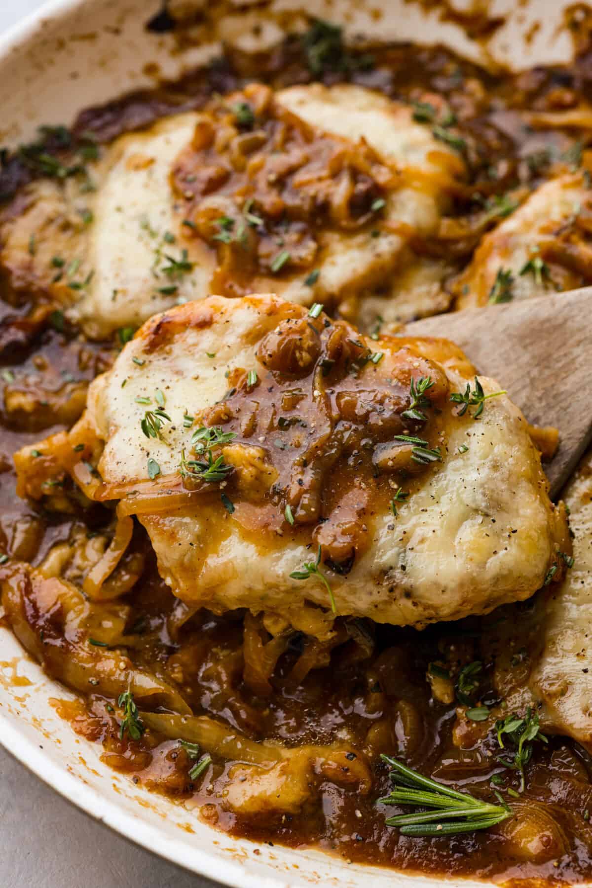 French Onion Pork Chops have all of the wonderful flavors of the classic soup in pork chop form! Caramelized onions and seared pork chops are joined with a savory sauce and two types of cheese for an amazing meal. Everything is cooked in one pan for a quick and easy weeknight dinner! A French onion pork chop on a wooden spoon