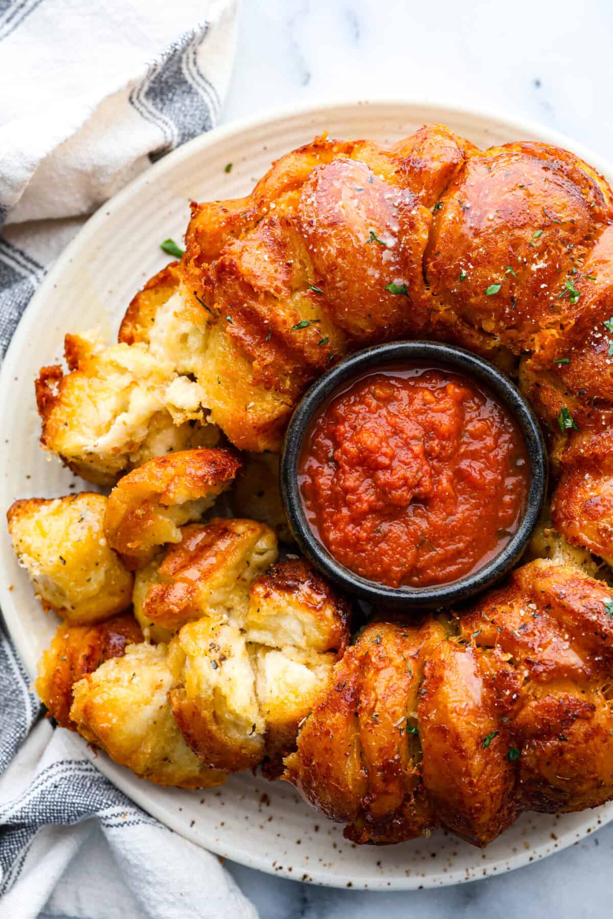 This garlic parmesan pull-apart bread is soft, flavorful, and beyond easy to make! It's filled with cheesy garlic flavor and is just the perfect size for dipping in all of your favorite sauces! Garlic parmesan pull-apart bread served around a bowl of marinara.