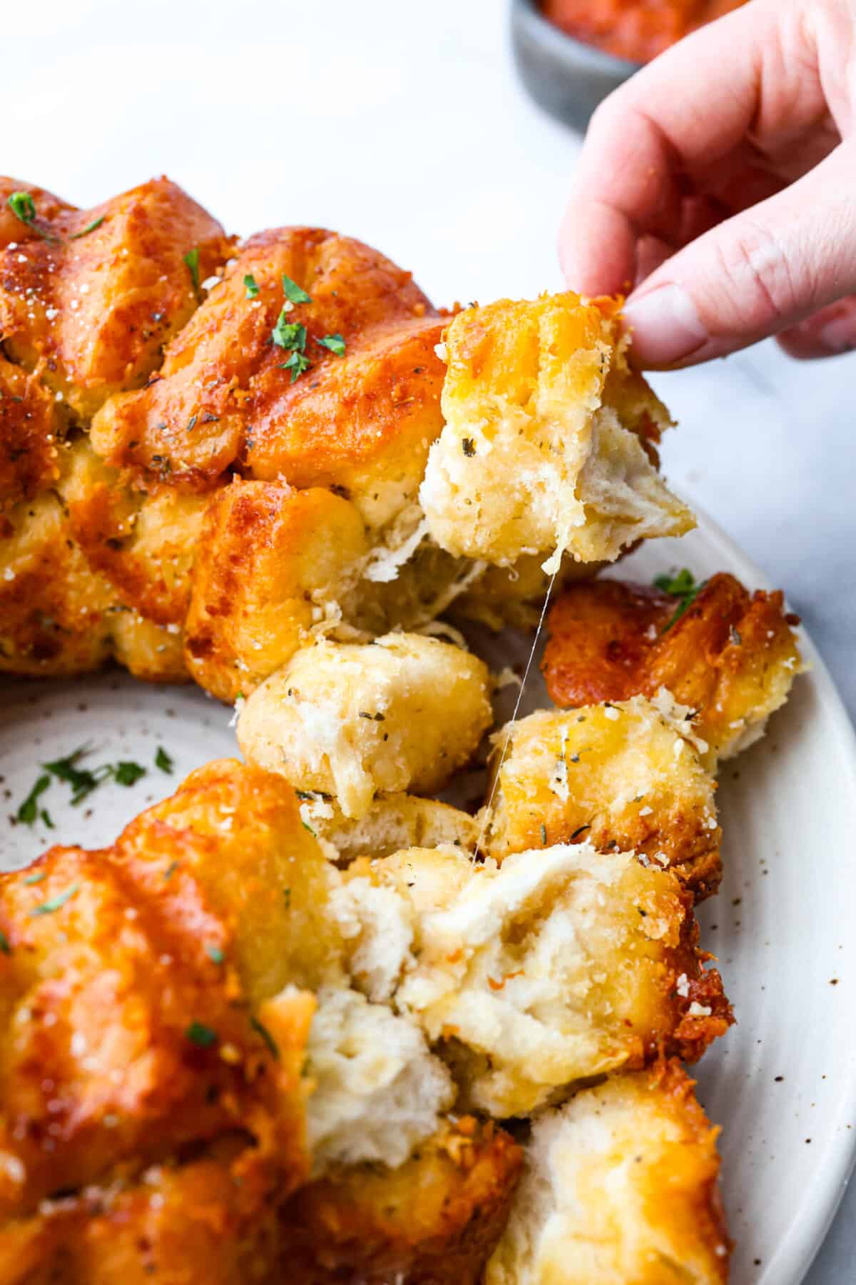 This garlic parmesan pull-apart bread is soft, flavorful, and beyond easy to make! It's filled with cheesy garlic flavor and is just the perfect size for dipping in all of your favorite sauces! Picking up a piece of garlic parmesan pull-apart bread.