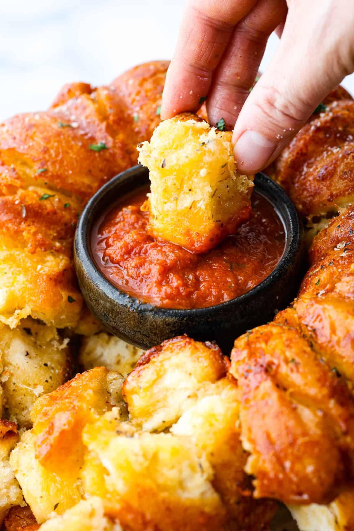 This garlic parmesan pull-apart bread is soft, flavorful, and beyond easy to make! It's filled with cheesy garlic flavor and is just the perfect size for dipping in all of your favorite sauces! Dipping a cheesy roll into the marinara sauce.