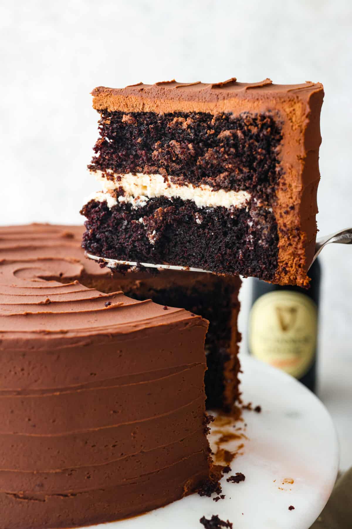 Celebrate St. Patrickโs Day (or any day) with this delicious Guinness Chocolate Cake! Itย has the most wonderful fudgy flavor and tender texture that is complemented by a Bailey's buttercream filling and a rich ganache frosting. Serving a slice of Guinness chocolate cake.