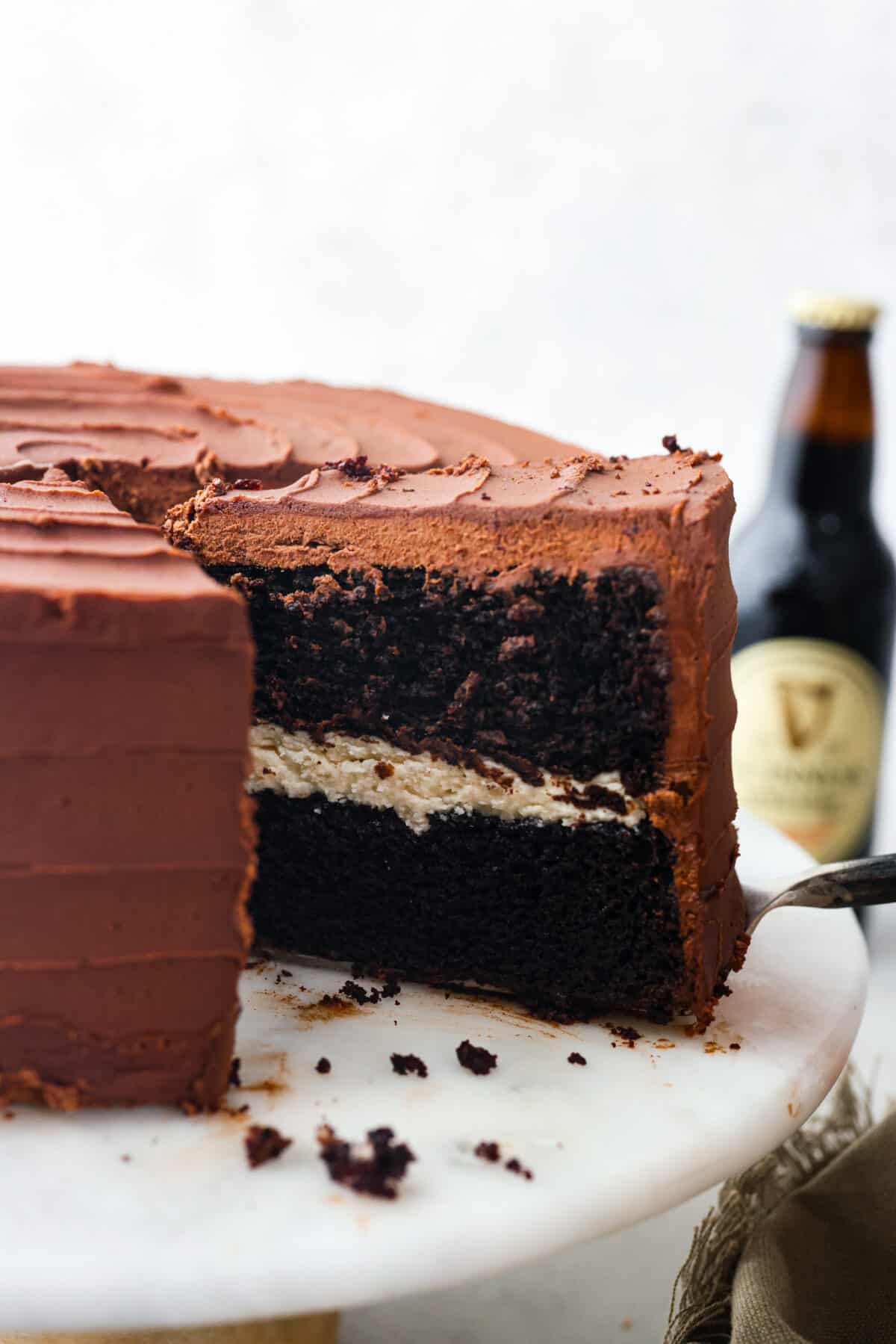 Celebrate St. Patrickโs Day (or any day) with this delicious Guinness Chocolate Cake! Itย has the most wonderful fudgy flavor and tender texture that is complemented by a Bailey's buttercream filling and a rich ganache frosting. Serving a slice of cake.