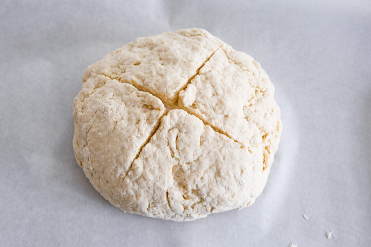 This Irish soda bread recipe uses just 4 pantry staples for a warm, crusty loaf that's perfect for slathering with butter and jam, or soaking up your favorite soup. No kneading required! An unbaked soda bread loaf, shaped and ready to be put in the oven.