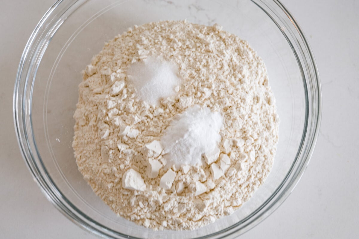 This Irish soda bread recipe uses just 4 pantry staples for a warm, crusty loaf that's perfect for slathering with butter and jam, or soaking up your favorite soup. No kneading required! Soda bread dough ingredients in a glass bowl.