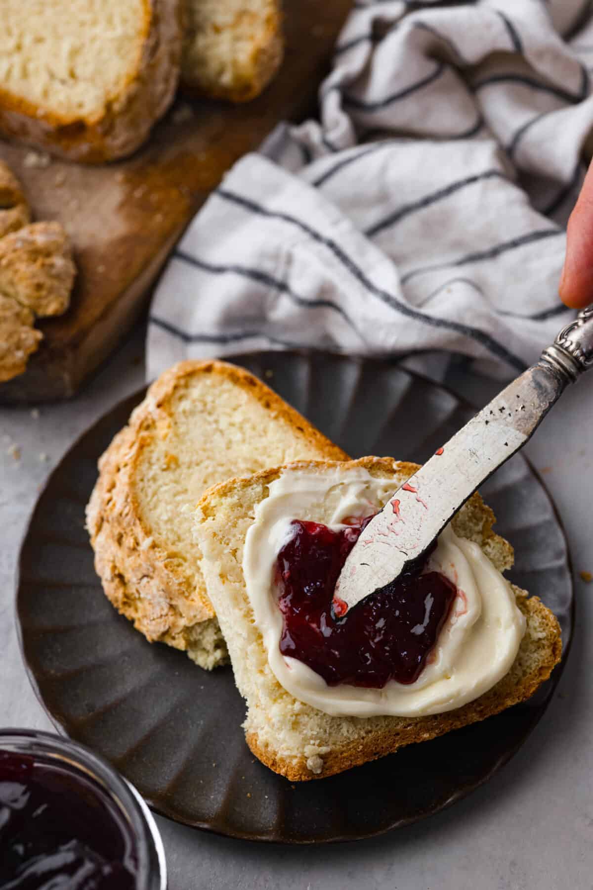 This Irish soda bread recipe uses just 4 pantry staples for a warm, crusty loaf that's perfect for slathering with butter and jam, or soaking up your favorite soup. No kneading required! Spreading butter and jam over a slice of bread.