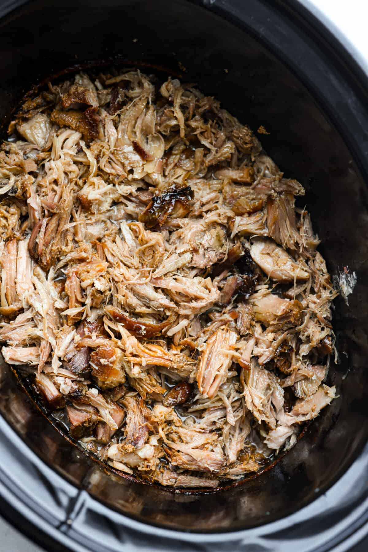Tender slow cooker kalua pulled pork is salty, smokey melt-in-your-mouth perfection. Enjoy authentic Hawaiian luau pork flavor at home with this super simple 3 ingredient masterpiece. Top view of the shredded kalua pork in the slow cooker.