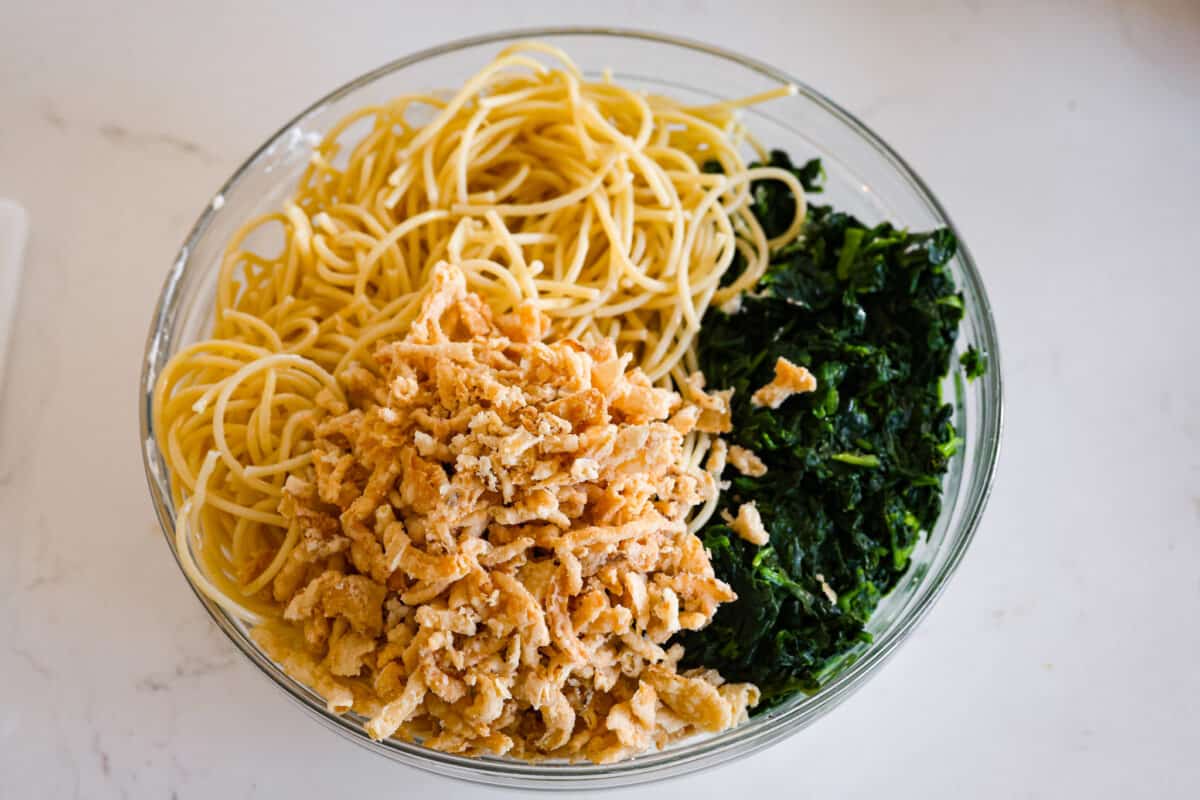 You will love the tasty flavors in this Monterey spaghetti! Tender spaghetti baked in a cheesy mixture and loaded with spinach and crispy fried onions. It's a surprisingly delicious combination of flavors and an easy weeknight dinner! Second process photo of spaghetti noodles, fried onions, and spinach in a bowl.