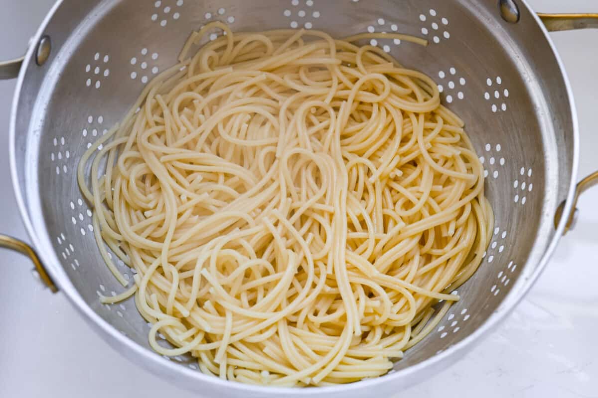 You will love the tasty flavors in this Monterey spaghetti! Tender spaghetti baked in a cheesy mixture and loaded with spinach and crispy fried onions. It's a surprisingly delicious combination of flavors and an easy weeknight dinner! First process photo of the spaghetti cooked and straining.