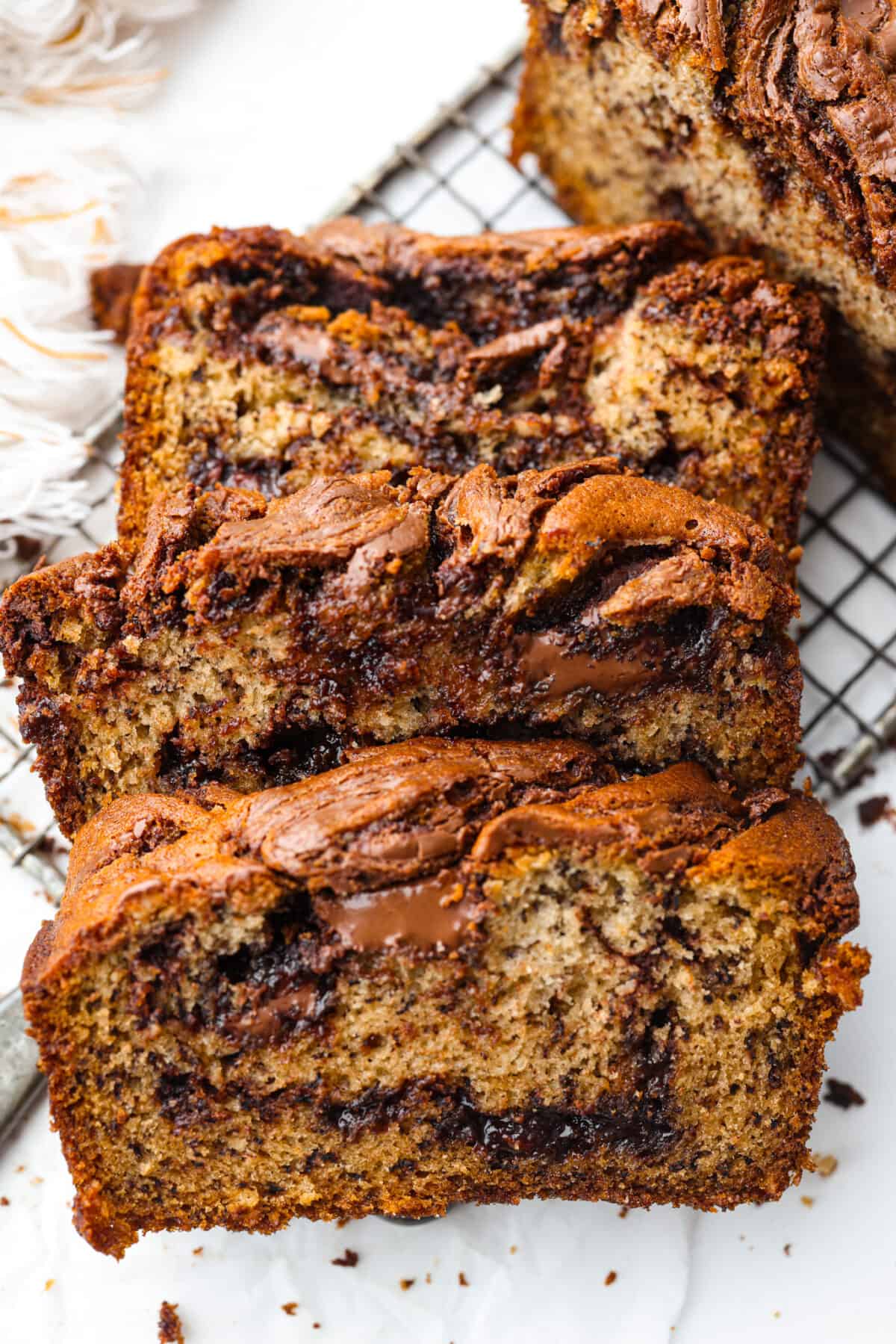 Treat yourself to the most incredible flavor and texture of this Nutella banana bread. One bite and you will be obsessed with the moist, tender crumb and how wonderful this quick bread tastes. It's a great way to use up ripe bananas and perfect for any occasion! 4 slices of Nutella banana bread on a wire rack.