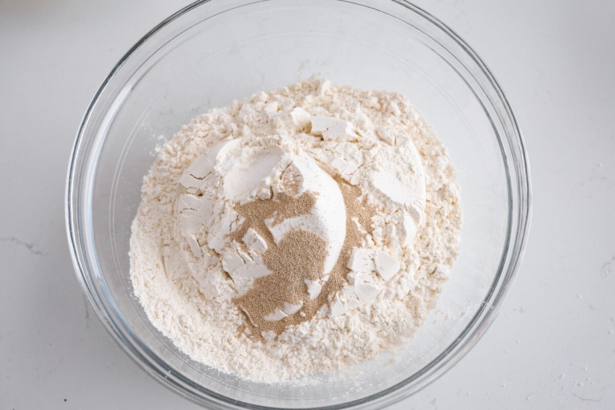 Make soft homemade bread without any kneading! This easy peasant bread recipe only uses 6 ingredients to make two perfect loaves of bread. Fluffy on the inside with a buttery golden crust on the outside. First process photo of dry ingredients in a bowl.