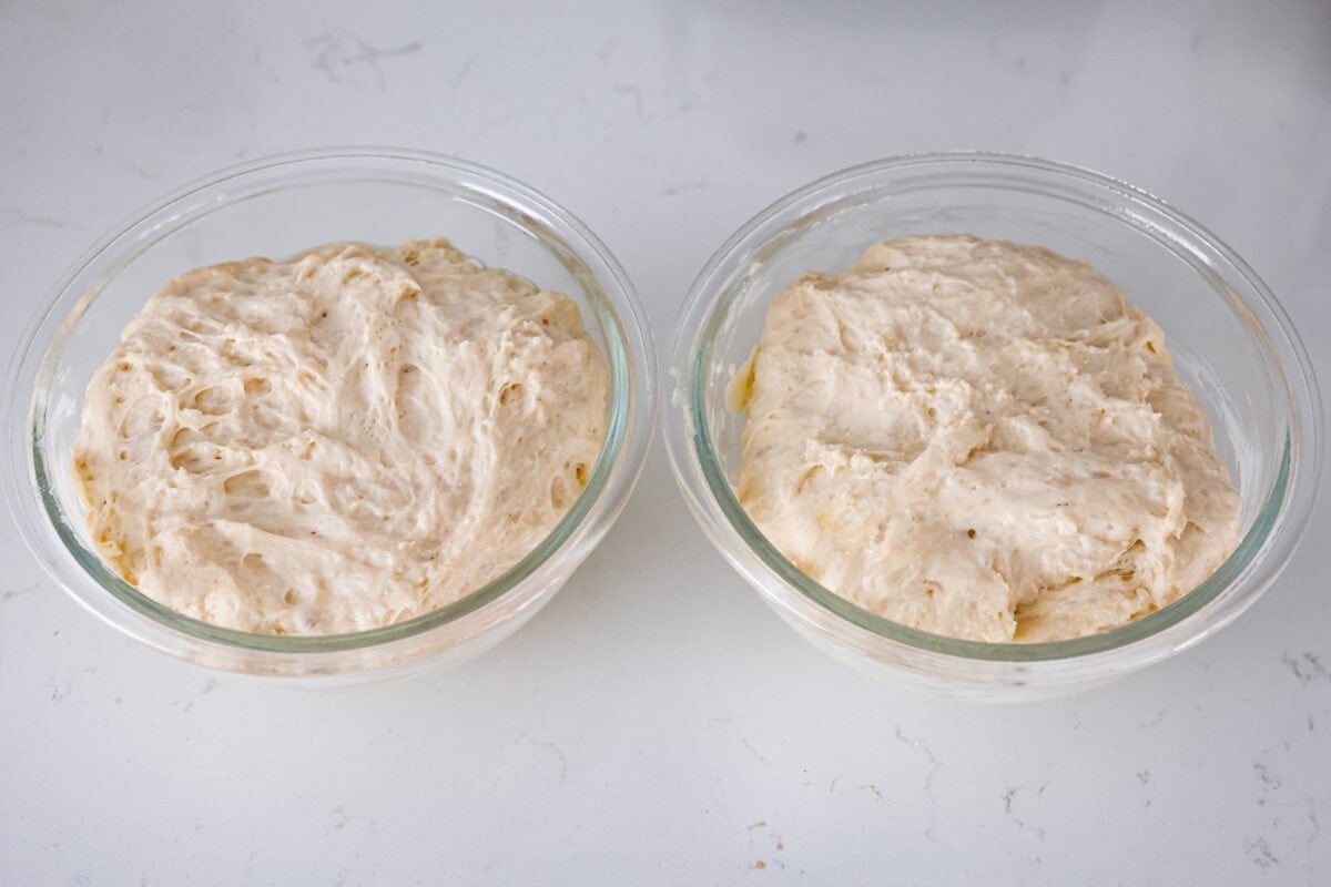 Make soft homemade bread without any kneading! This easy peasant bread recipe only uses 6 ingredients to make two perfect loaves of bread. Fluffy on the inside with a buttery golden crust on the outside. Fourth process photo of the peasant bread dough divided into the prepared bowls.