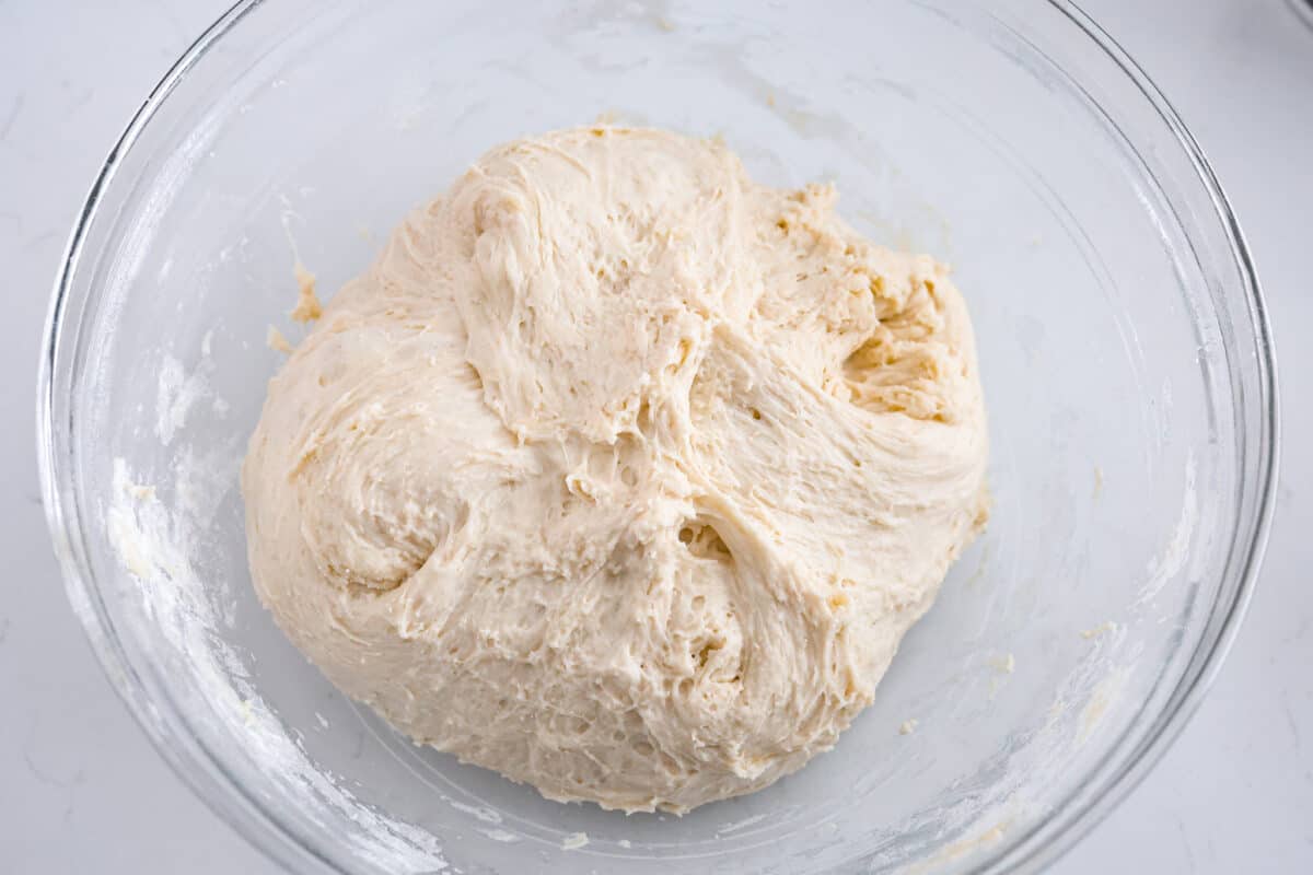 Make soft homemade bread without any kneading! This easy peasant bread recipe only uses 6 ingredients to make two perfect loaves of bread. Fluffy on the inside with a buttery golden crust on the outside. Third process photo of the mixed dough in a bowl before it rises.