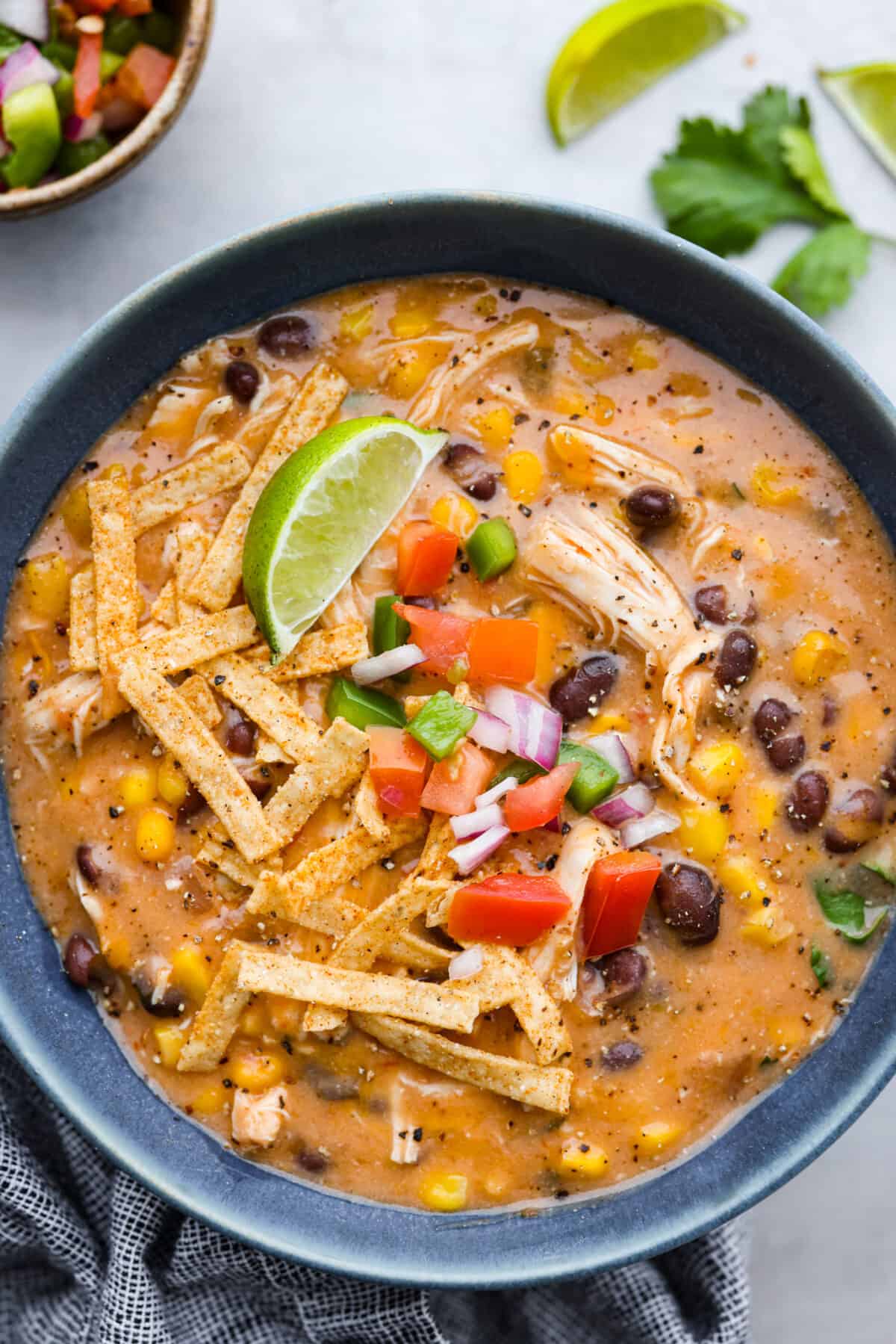 Everything you love about fajitas comes together in this hearty Slow Cooker Chicken Fajita Soup. Tender chicken surrounded by beans, corn, and spices simmers all day to perfection A serving of chicken fajita soup, topped with tortilla strips, diced tomatoes, and a lime wedge.
