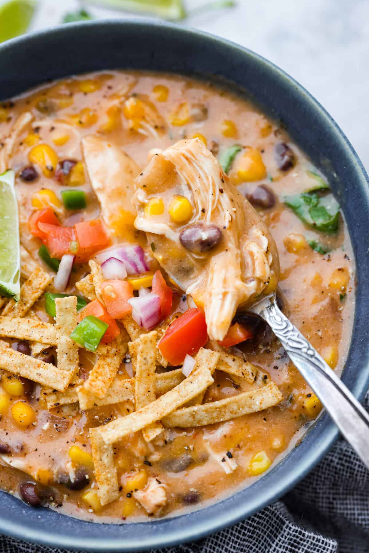Everything you love about fajitas comes together in this hearty Slow Cooker Chicken Fajita Soup. Tender chicken surrounded by beans, corn, and spices simmers all day to perfection Close-up of the soup in a gray bowl.