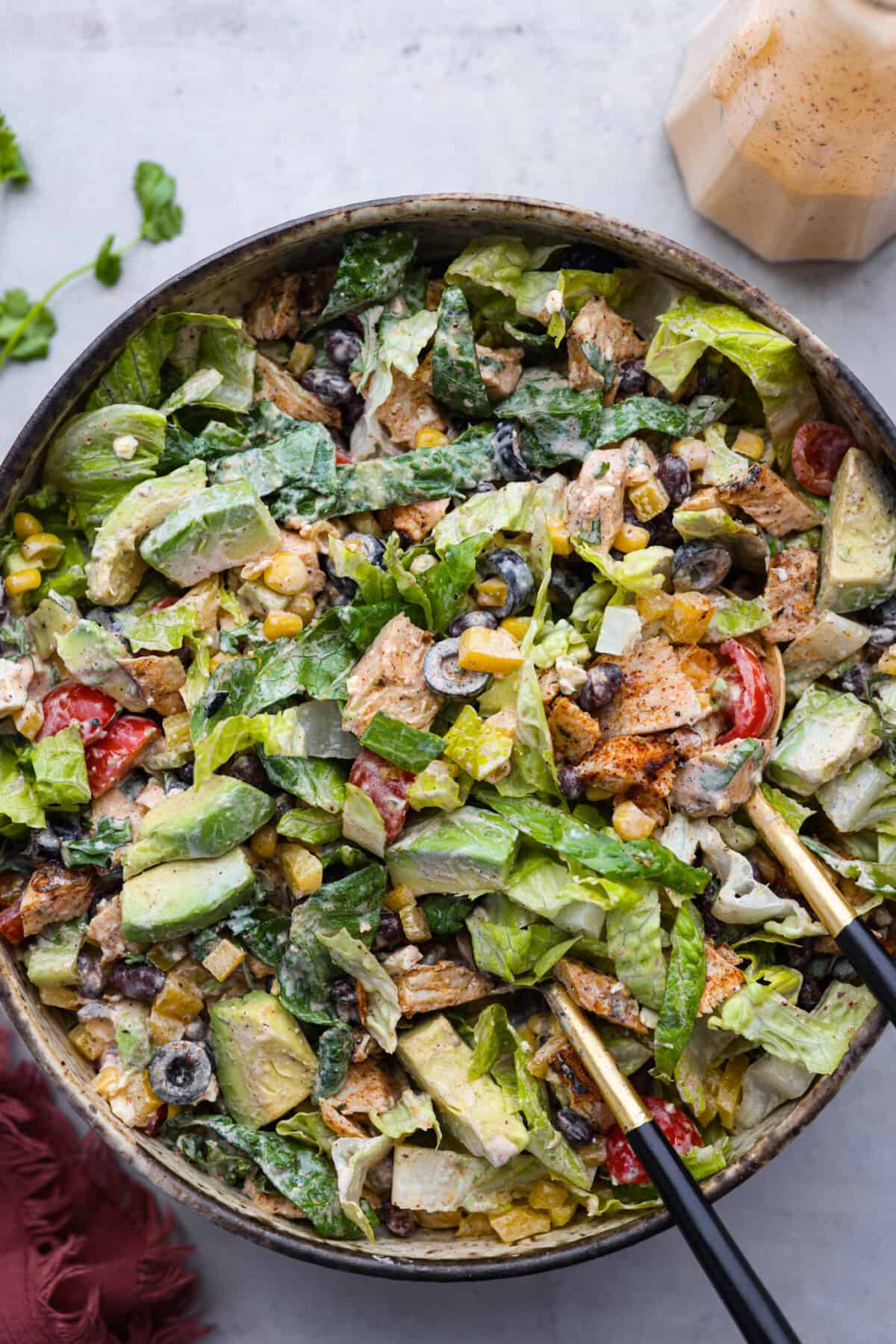 Santa Fe Salad is filled with bold southwestern flavor and has the most wonderful texture. Romaine lettuce, grilled chicken, black beans, corn, tomatoes, tortilla strips, avocado and cheese come together for the most amazing combination. And the creamy southwest dressing is the perfect finishing touch. Hero image of santa fe salad in a large mixing bowl.