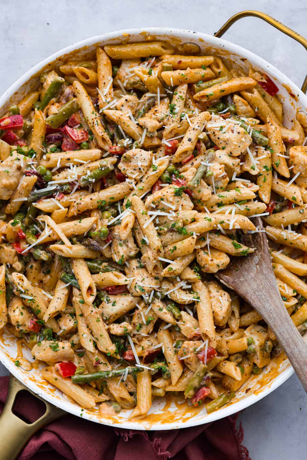 Spicy chicken chipotle pasta is so creamy and rich with a spicy kick that you won't be able to get enough of. The warm, smoky flavor of the chipotle peppers balanced with a flavorful cream sauce is sure to delight your tastebuds! It is a mouthwatering entree that everyone will love! Inspired by Cheesecake Factory, this homemade version is so tasty! Top-down view of chipotle pasta in a white skillet with a gold handle. It is being stirred with a wooden spoon.