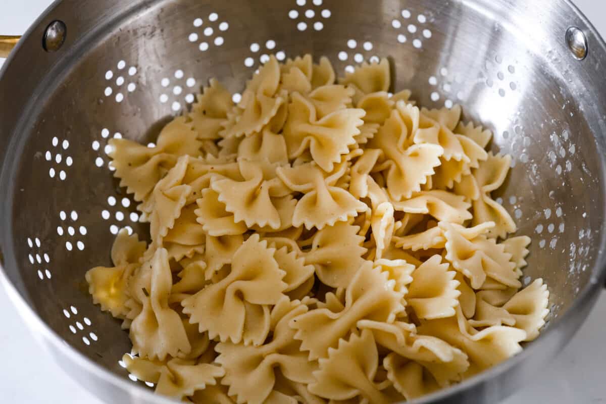 Teriyaki spinach pasta salad combines juicy mandarin oranges, savory teriyaki chicken, and crunchy cashews for a flavor explosion in every bite! The best Asian-inspired pasta salad to serve alongside your favorite meals. The cooked bowtie pasta being strained.