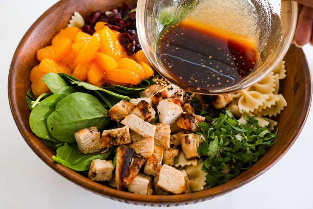 Teriyaki spinach pasta salad combines juicy mandarin oranges, savory teriyaki chicken, and crunchy cashews for a flavor explosion in every bite! The best Asian-inspired pasta salad to serve alongside your favorite meals. Adding the dressing to the teriyaki spinach pasta salad.