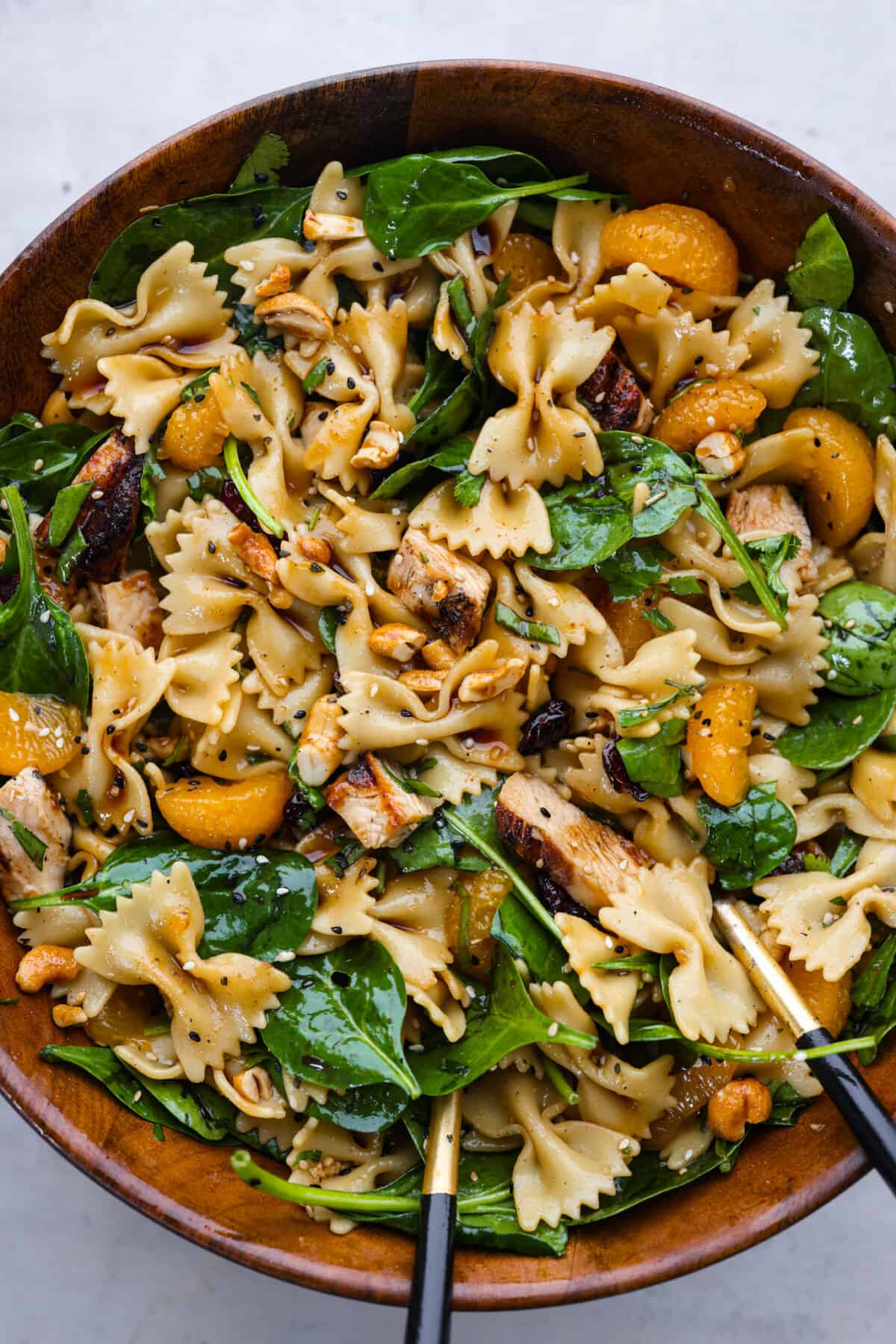 Teriyaki spinach pasta salad combines juicy mandarin oranges, savory teriyaki chicken, and crunchy cashews for a flavor explosion in every bite! The best Asian-inspired pasta salad to serve alongside your favorite meals. Teriyaki spinach pasta salad served in a large wooden serving bowl.