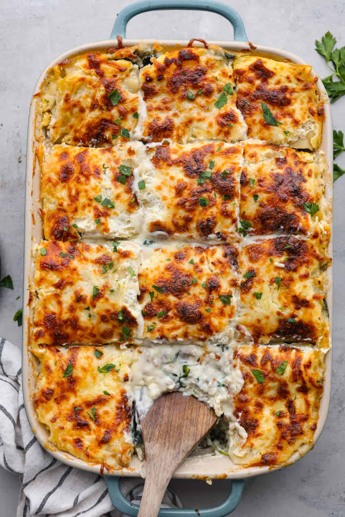This white lasagna recipe swaps out traditional marinara for a homemade alfredo sauce that’s too good to resist. Packed with tender spinach, ricotta cheese, and Italian sausage, each bite is a dream! Top-down view of white lasagna cut into squares.