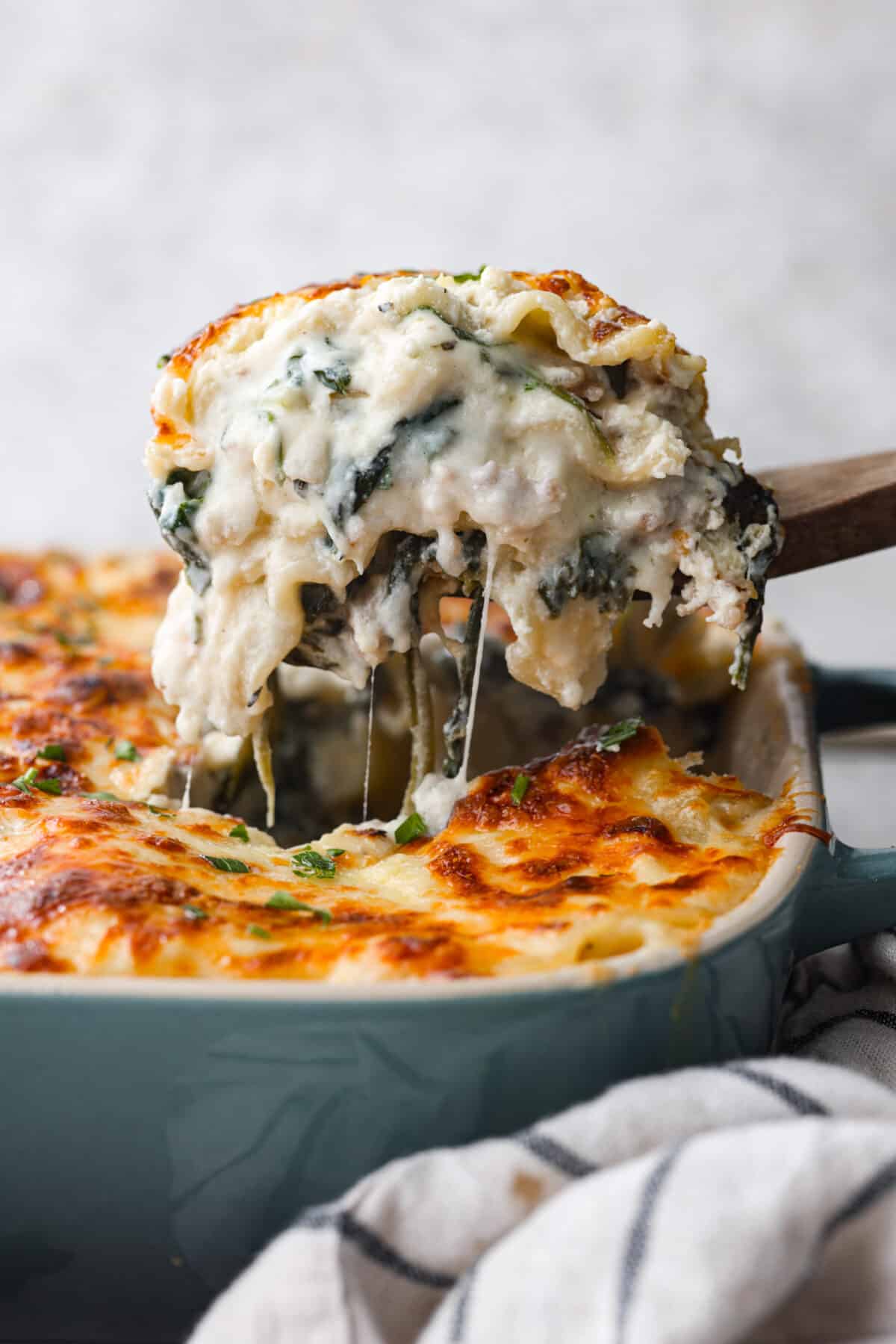 This white lasagna recipe swaps out traditional marinara for a homemade alfredo sauce that’s too good to resist. Packed with tender spinach, ricotta cheese, and Italian sausage, each bite is a dream! Scooping up lasagna with a wooden spoon.