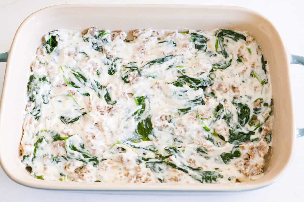 This white lasagna recipe swaps out traditional marinara for a homemade alfredo sauce that’s too good to resist. Packed with tender spinach, ricotta cheese, and Italian sausage, each bite is a dream! Adding the white sauce layer to a baking dish.