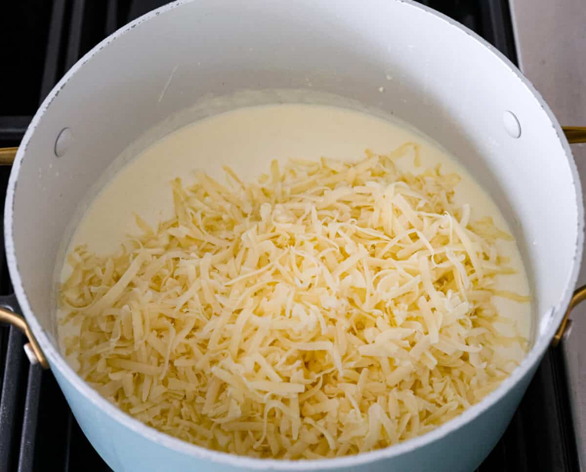 White Cheddar Mac and Cheese is super creamy and filled with rich, decadent flavor. This pasta recipe is the perfect comforting side dish for potlucks, holidays or even weeknight dinners! The cheesy sauce being melted together in a large pot.