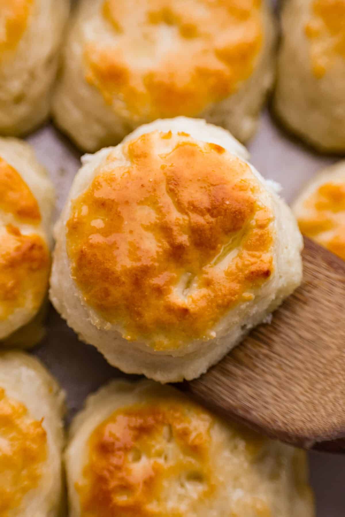 Tender and fluffyย 7-up biscuitsย rise to perfection and instantly become everyone's favorite biscuit! It only takes 4-ingredients to create this melt-in-your-mouth biscuit recipe! Close view of a biscuit on a wood spatula.