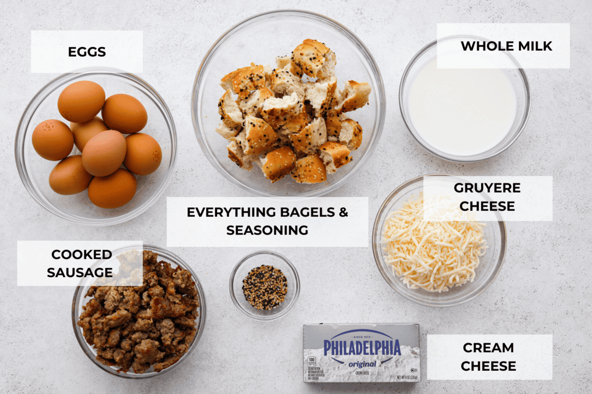 Wake up to the tasty flavors of this everything bagel casserole! It's made with everything bagels and seasoning, sausage, eggs, cream cheese, and gruyère cheese. The result is a creamy and savory breakfast casserole that everyone will devour! Top view of labeled ingredients to make everything bagel casserole.